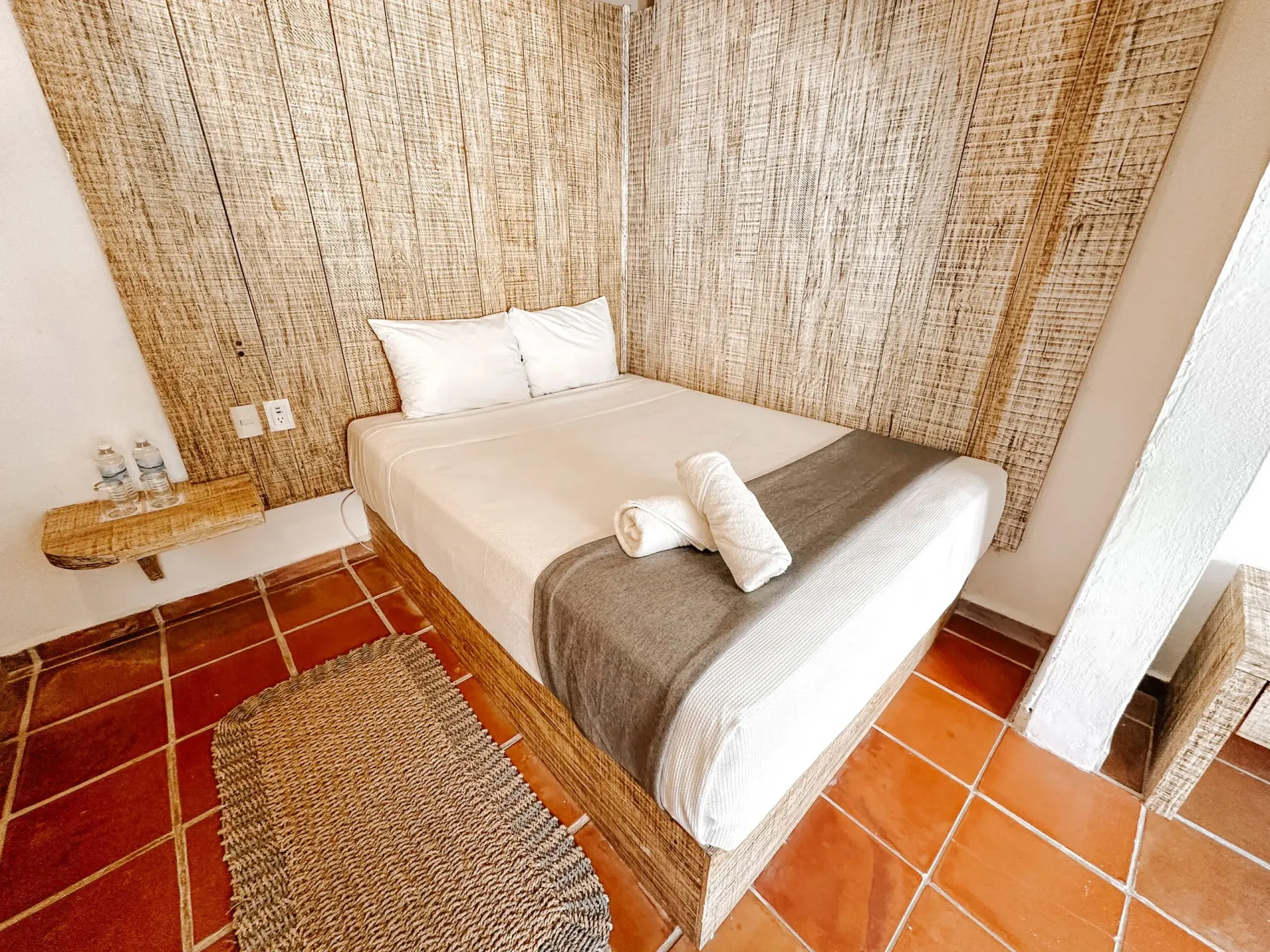 Dormitorio con pared tejida, cama con ropa de cama blanca y suelo de baldosas.