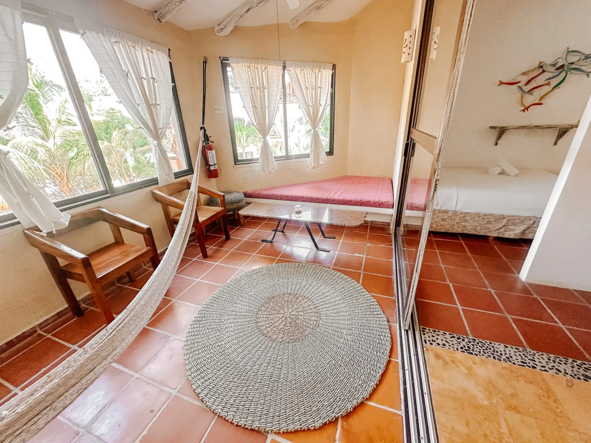 Habitación con hamaca, cama, ventana y alfombra; interior en tonos tierra.