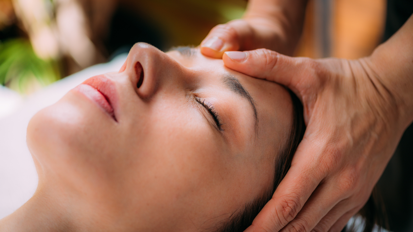 Person receiving a head massage with hands gently resting on their forehead and temples; eyes closed.