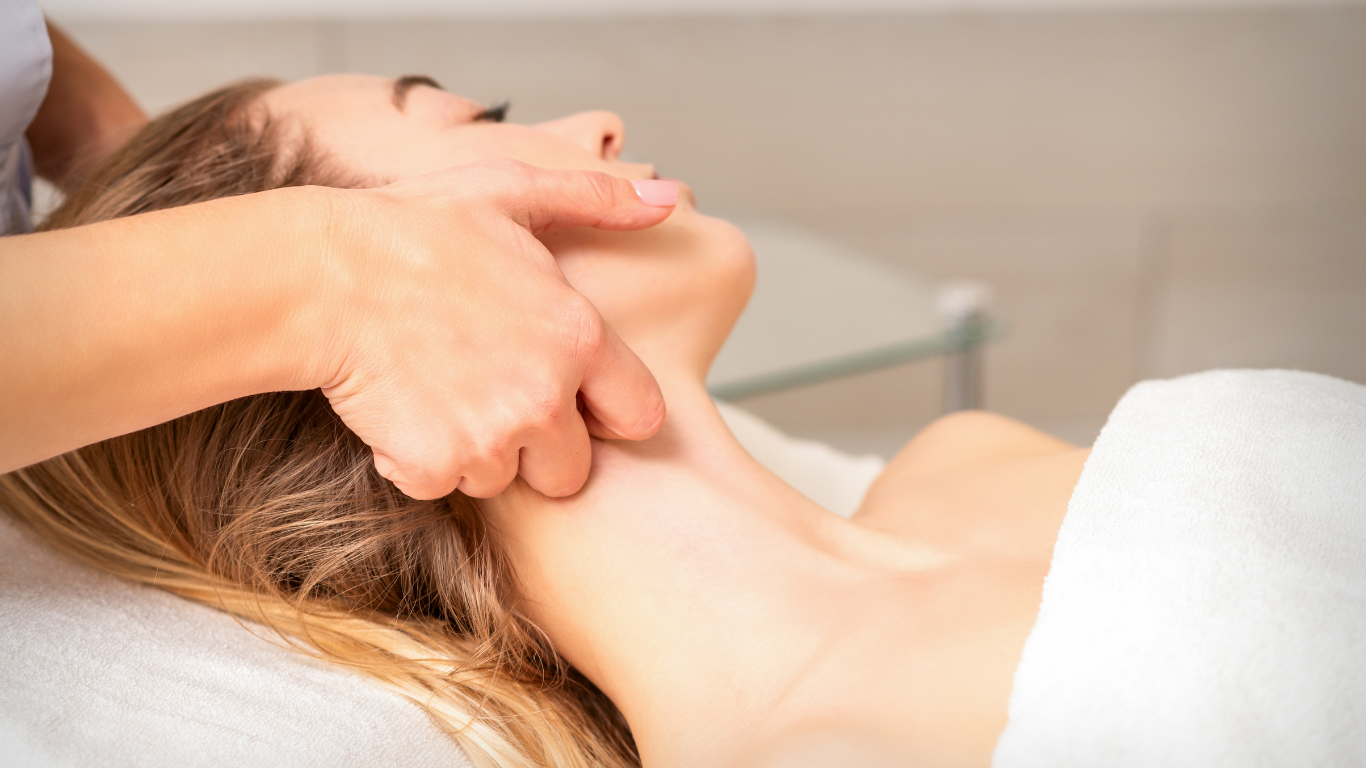 Woman receiving neck massage in a spa setting, lying down, hand on her neck.