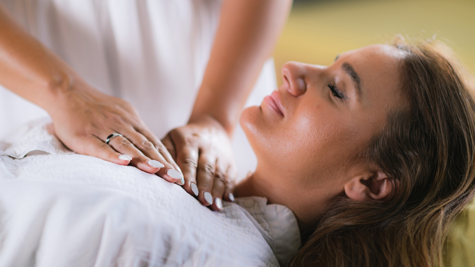 Person receiving a healing session with hands on chest; light-colored clothing; relaxed expression.