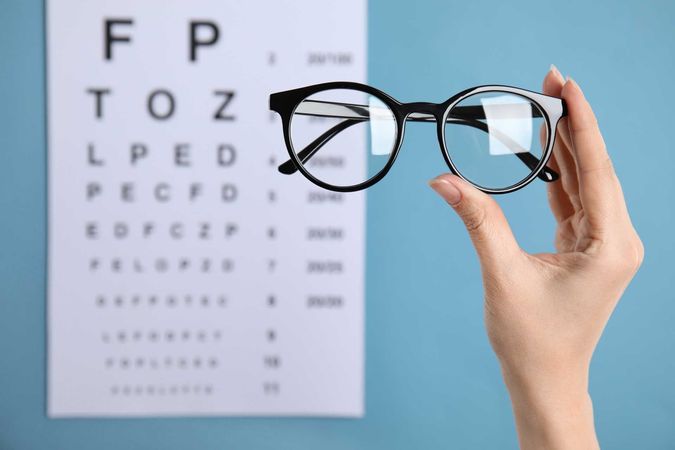 A person is holding a pair of glasses in front of an eye chart.