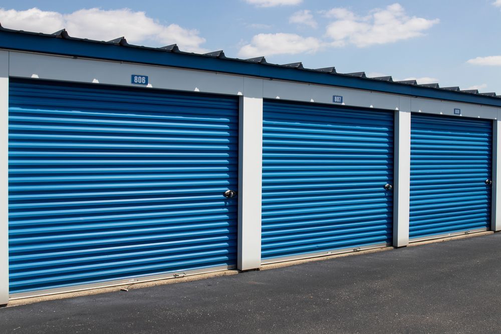 Three blue storage unit doors in a row, with a blue sky background.