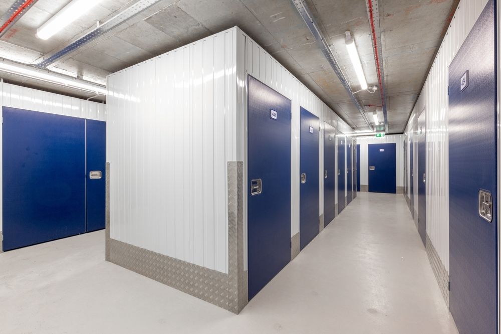 Hallway with blue storage unit doors. White walls and floor, fluorescent lights, and concrete ceiling.