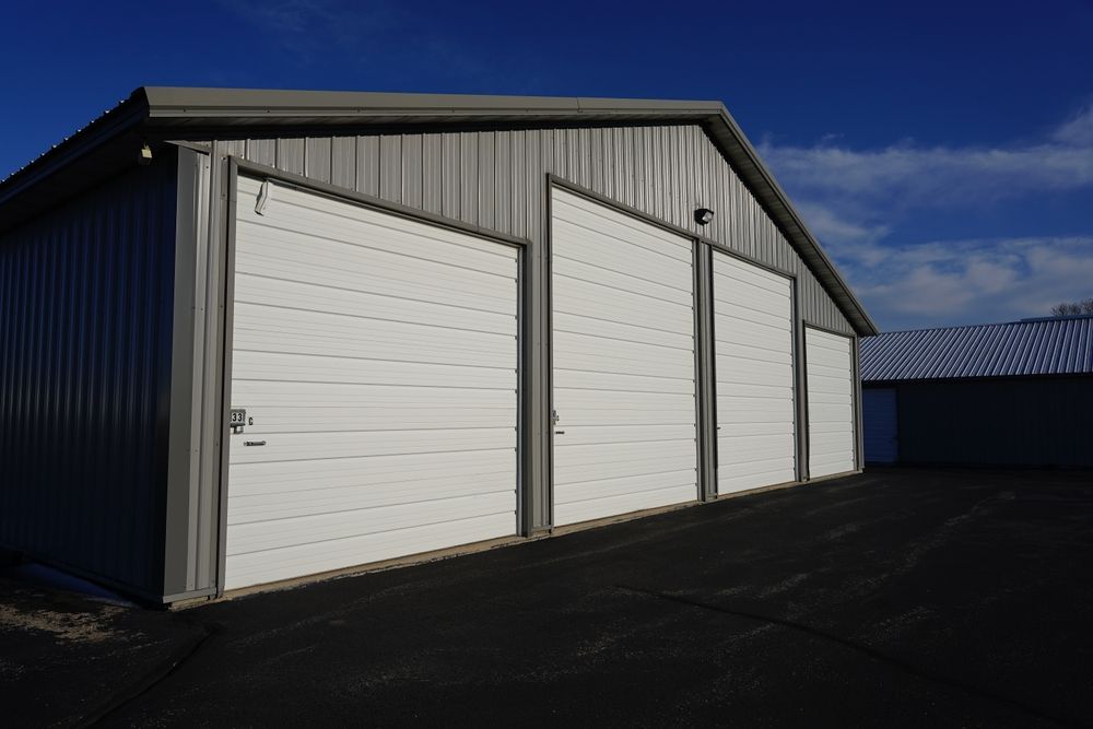 Gray metal storage building with three white garage doors against a blue sky.