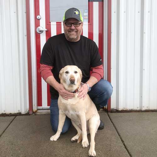 A man is kneeling down next to a dog in front of a door.