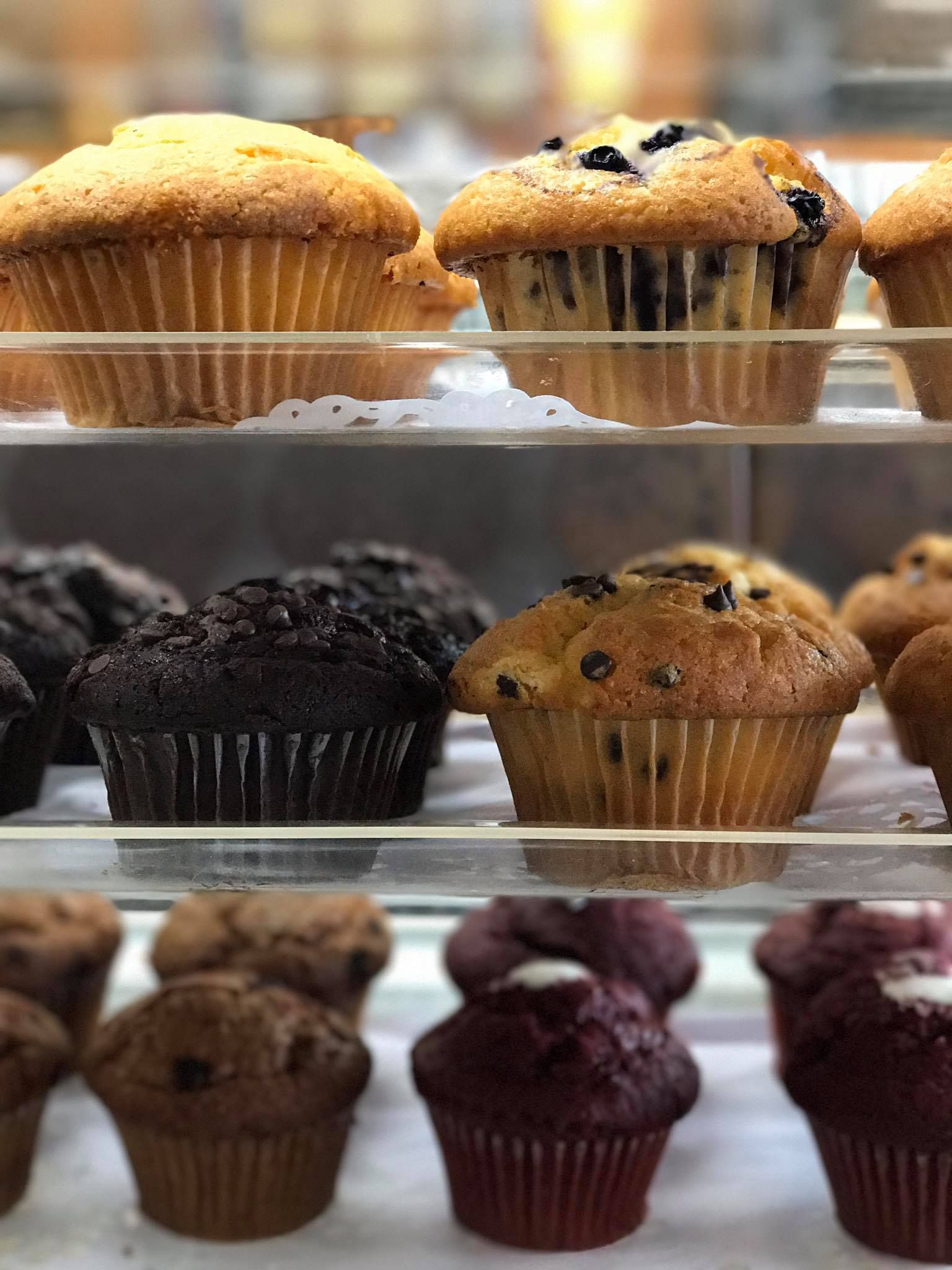 A variety of muffins are displayed on a glass shelf.