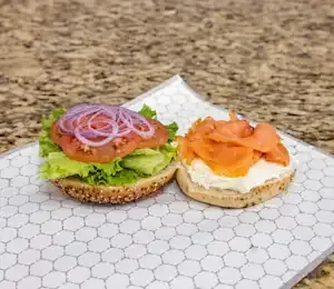 Two bagels with smoked salmon, lettuce, tomatoes, and onions on them are sitting on a table.