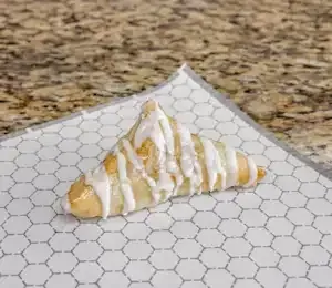 A triangle-shaped pastry with icing on it is sitting on a piece of wax paper.