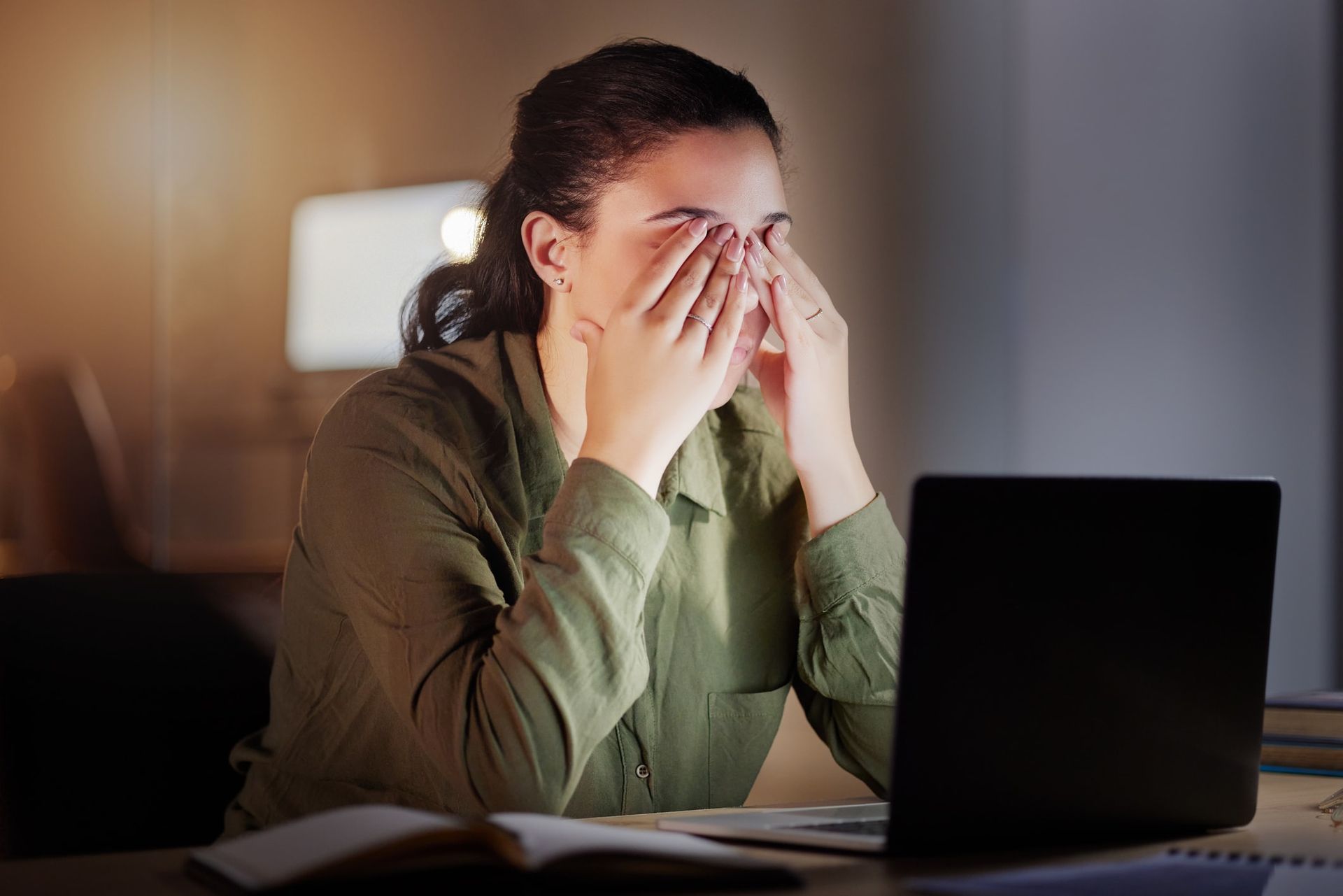 A woman is rubbing her eyes while sitting in front of a laptop computer.