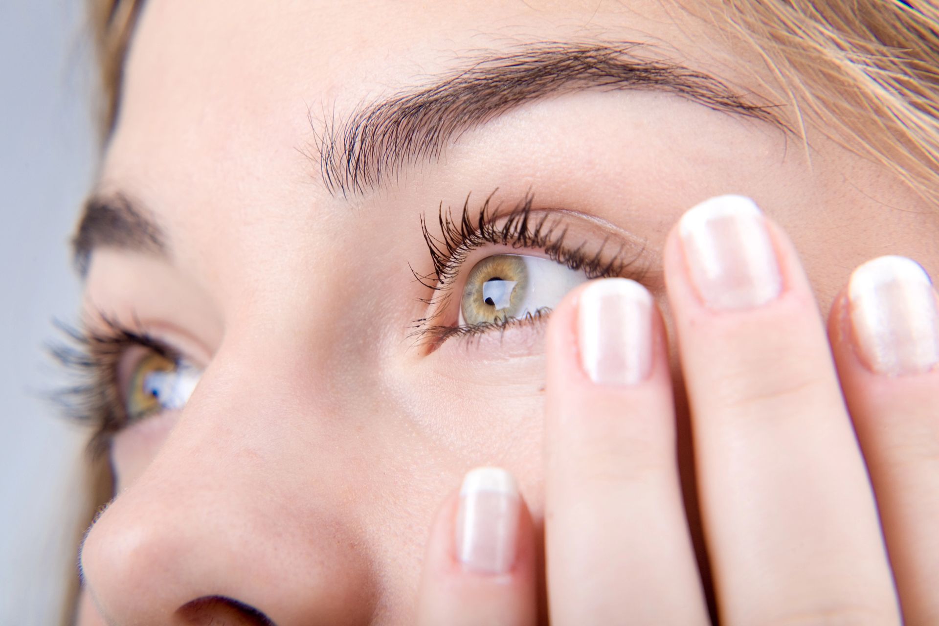 A close up of a woman covering her eye with her hands.