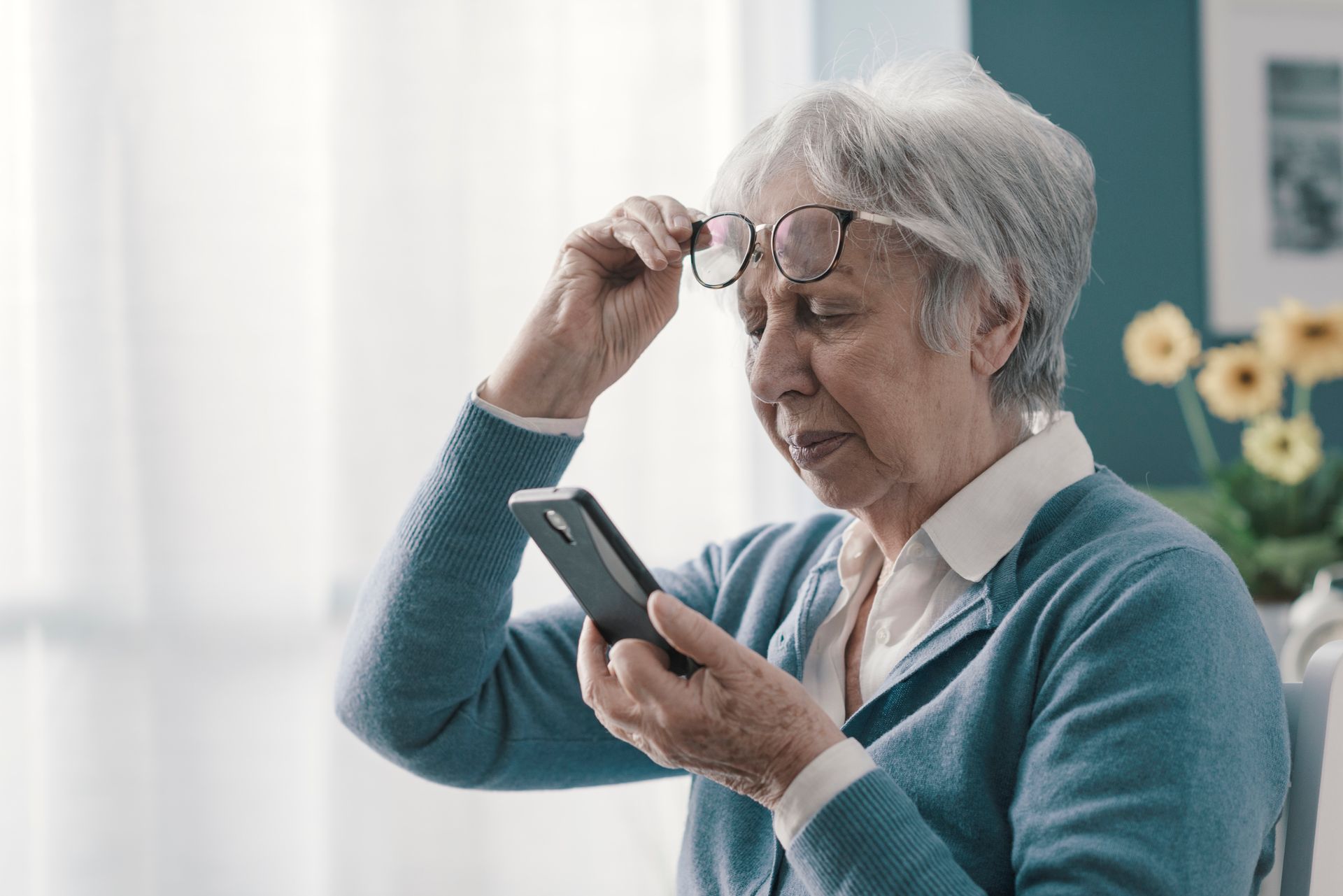 An elderly woman wearing glasses is looking at her cell phone.