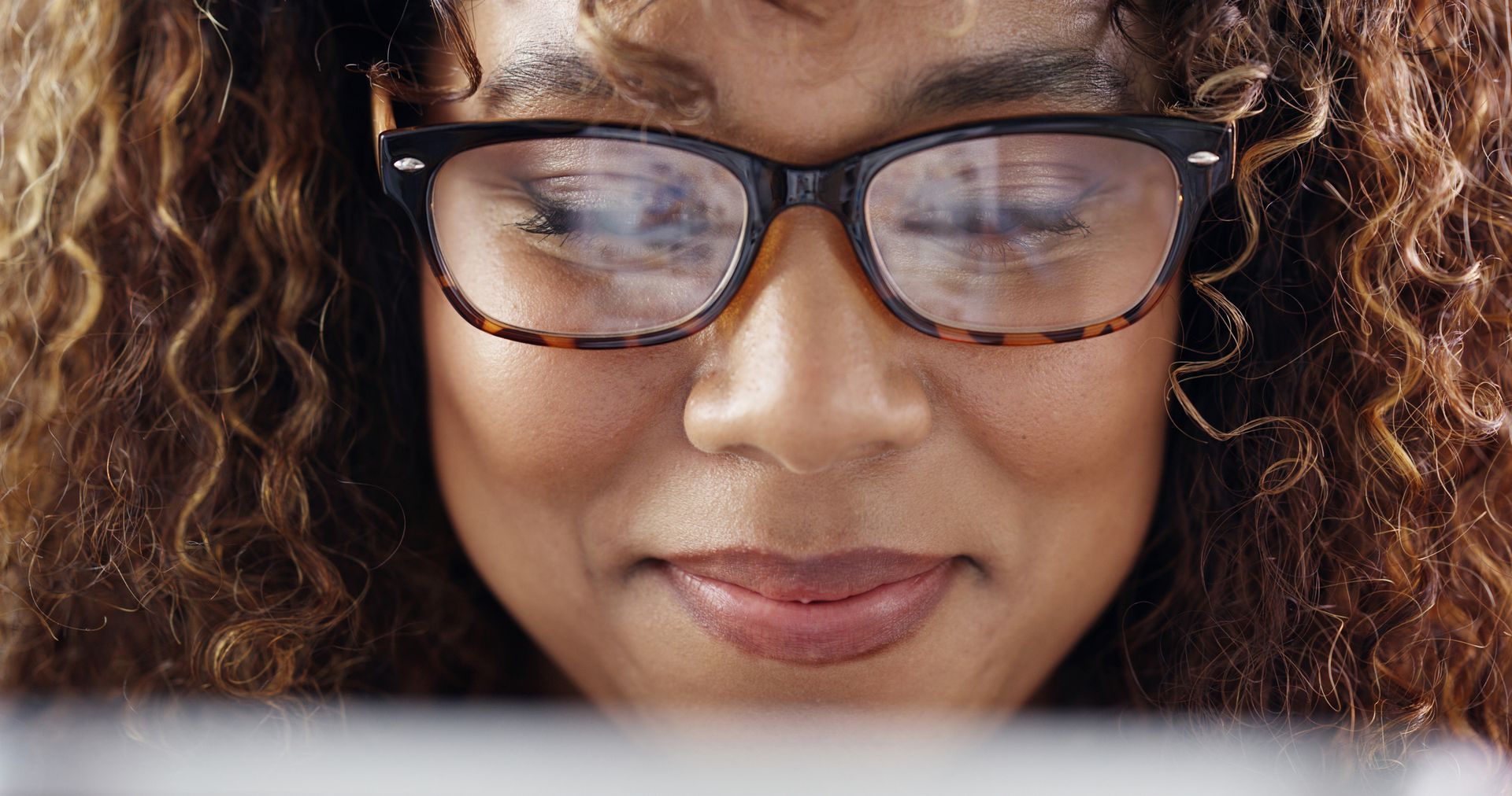 Close-up of a smiling person wearing glasses, looking down at a screen.