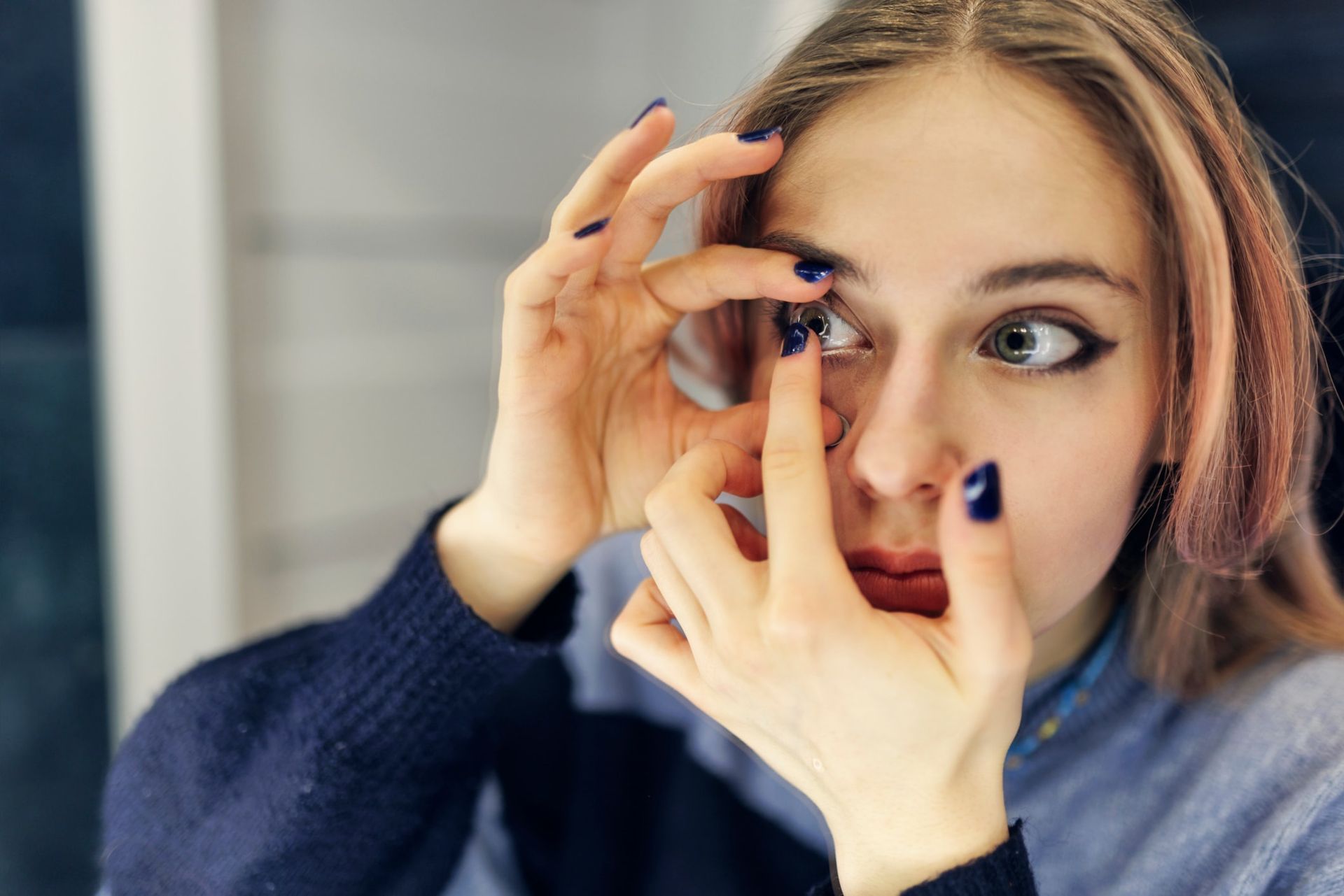 A woman is putting contact lenses in her eye.