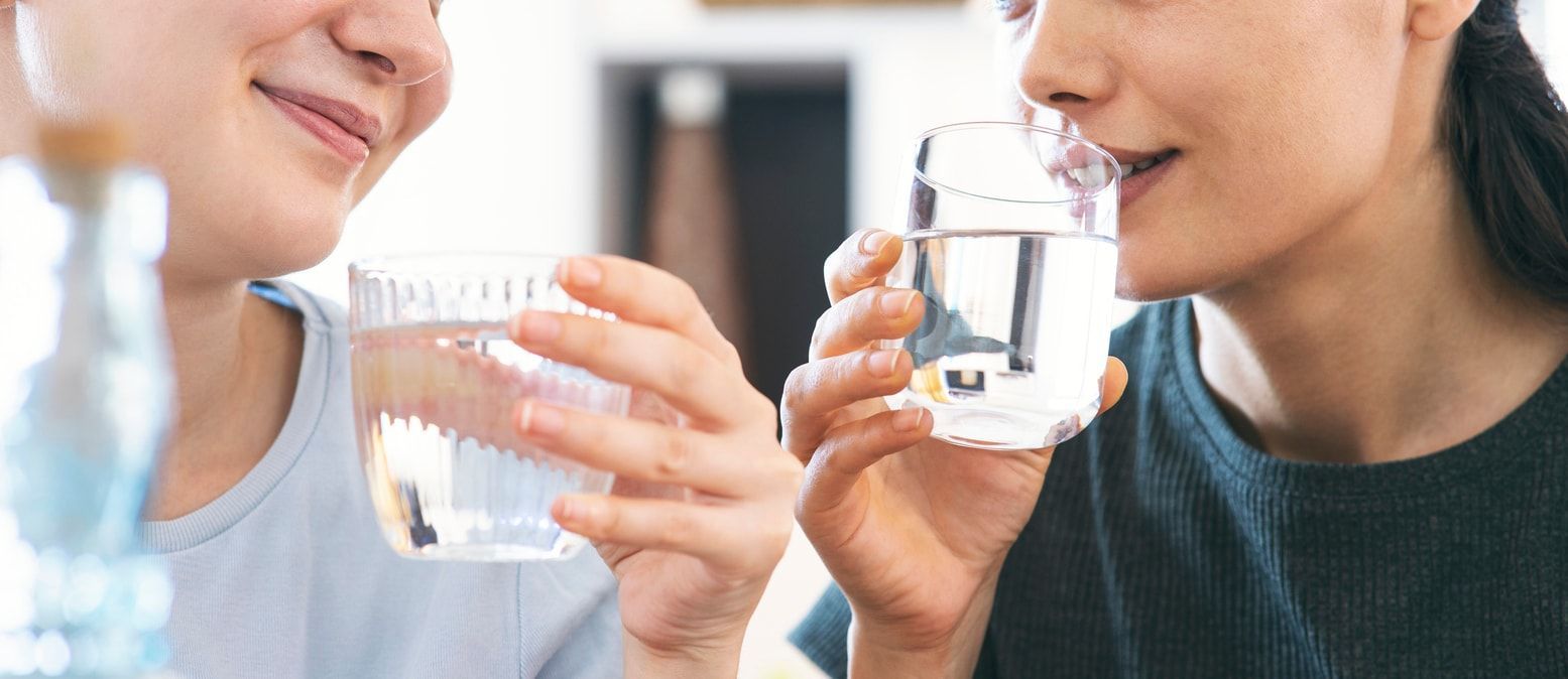 Two women are drinking water from glasses while sitting at a table.