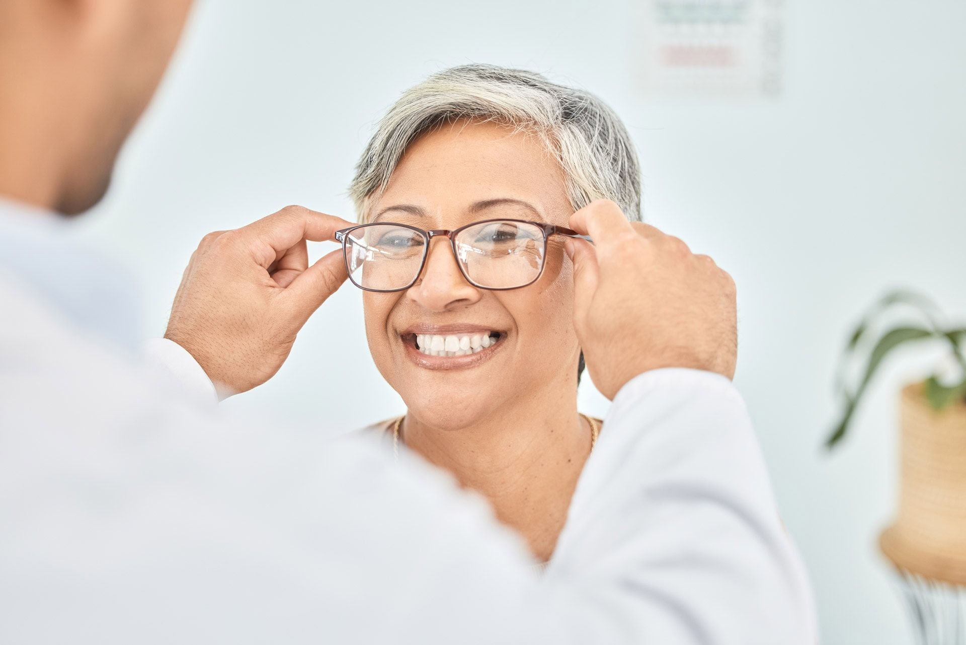 Person fitting glasses on a smiling woman in a bright clinic setting