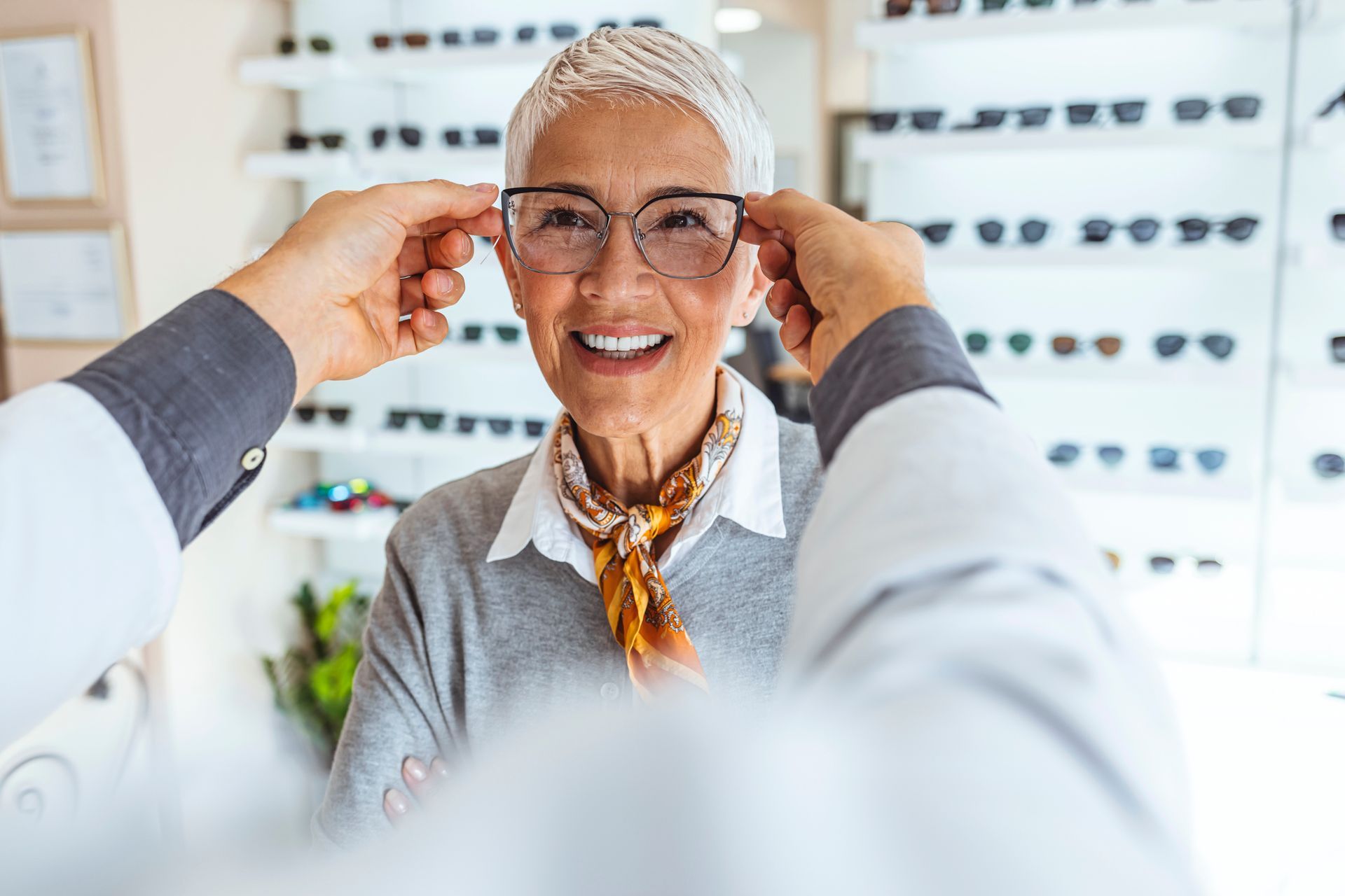 A person in an optician's office helping a client try on a pair of new eyeglasses.