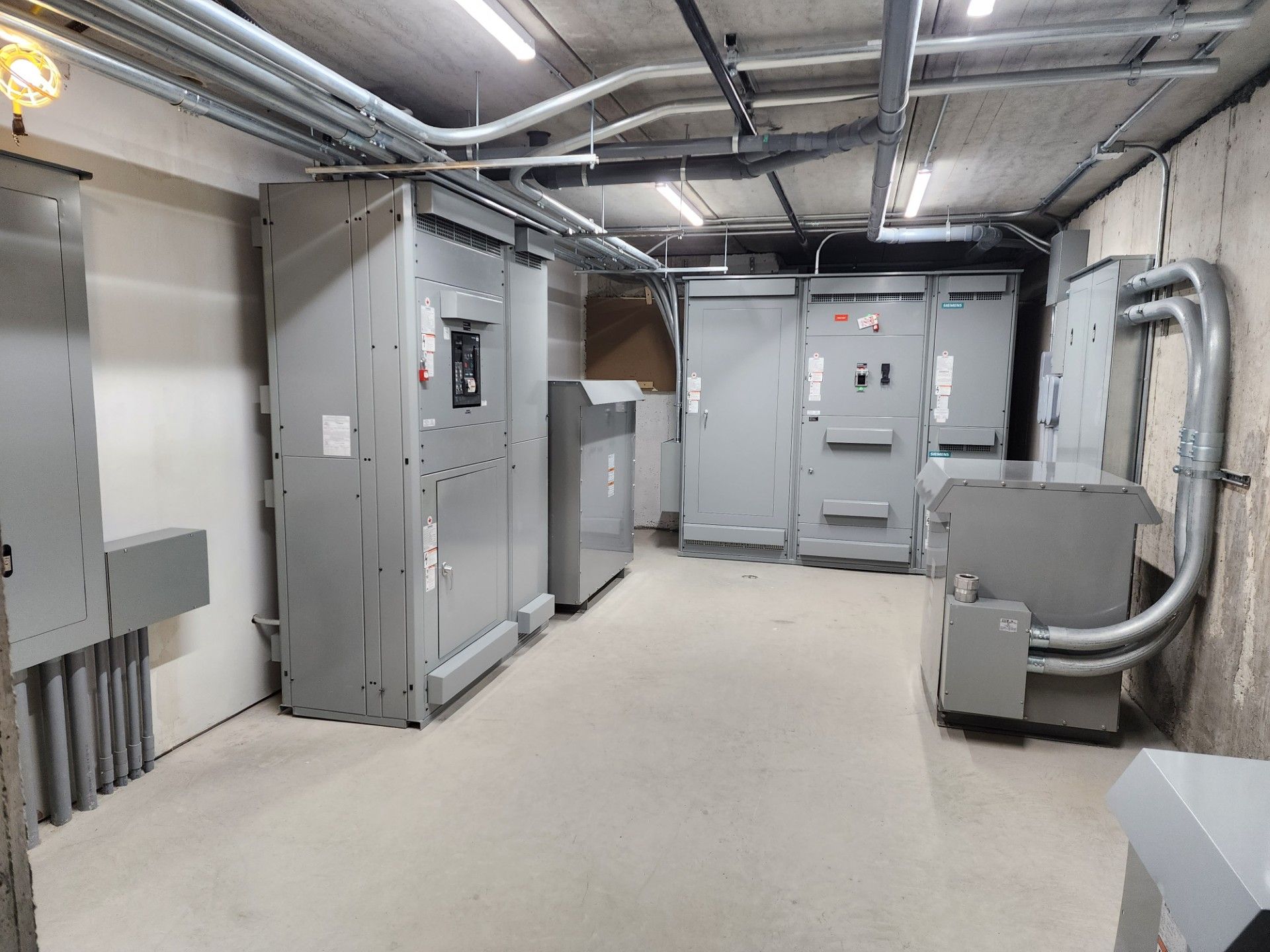 Electrical equipment room with several large gray metal cabinets and conduit on walls and ceiling.