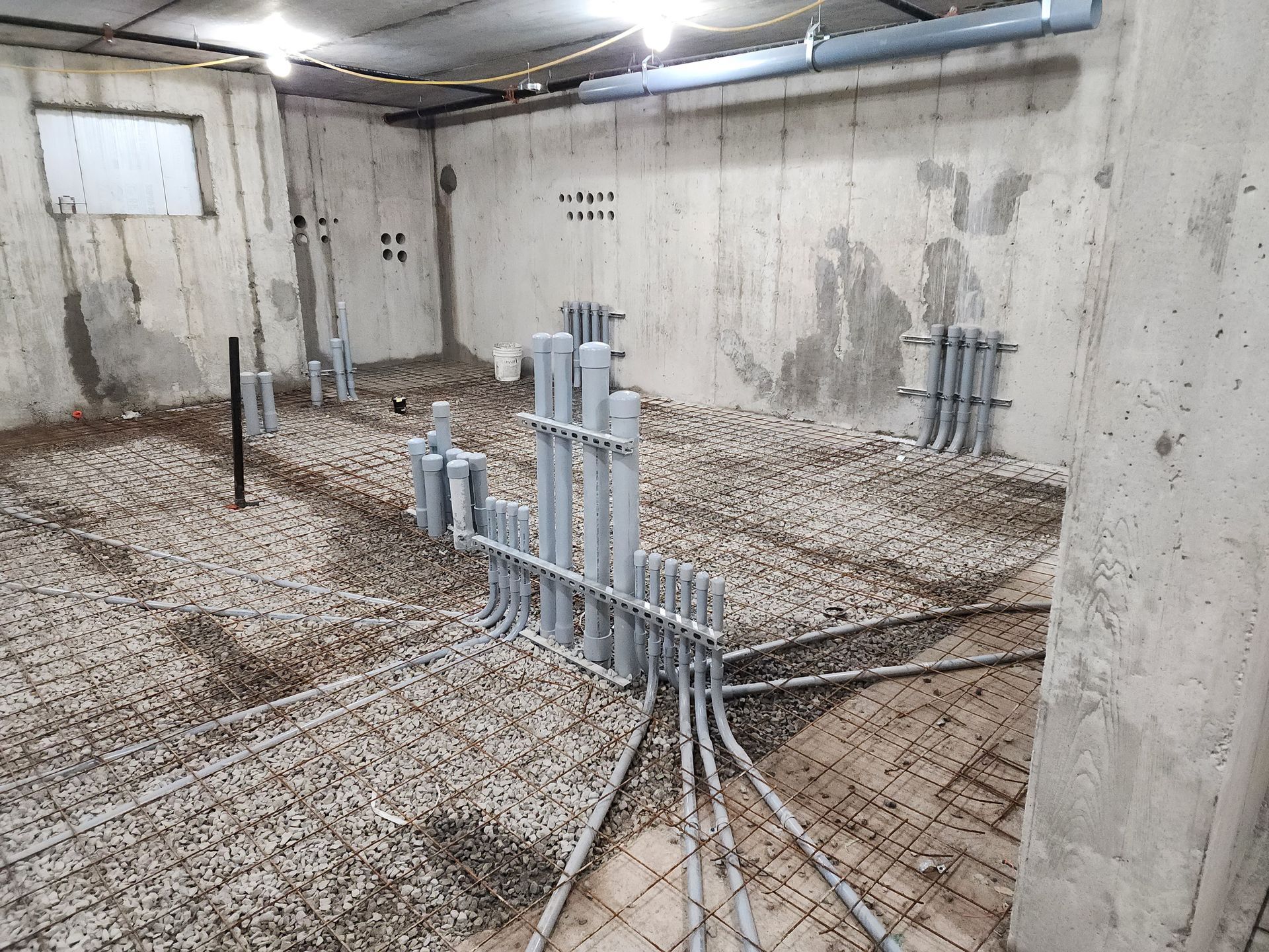Concrete room with electrical conduits and rebar for flooring. Walls have embedded pipes, ready for construction.