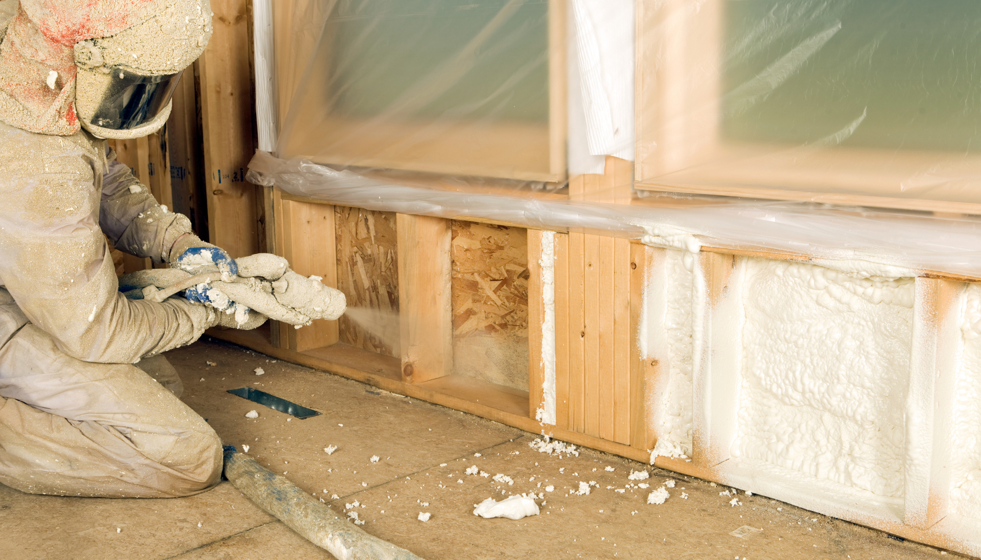 A man is spraying foam insulation on a wall.