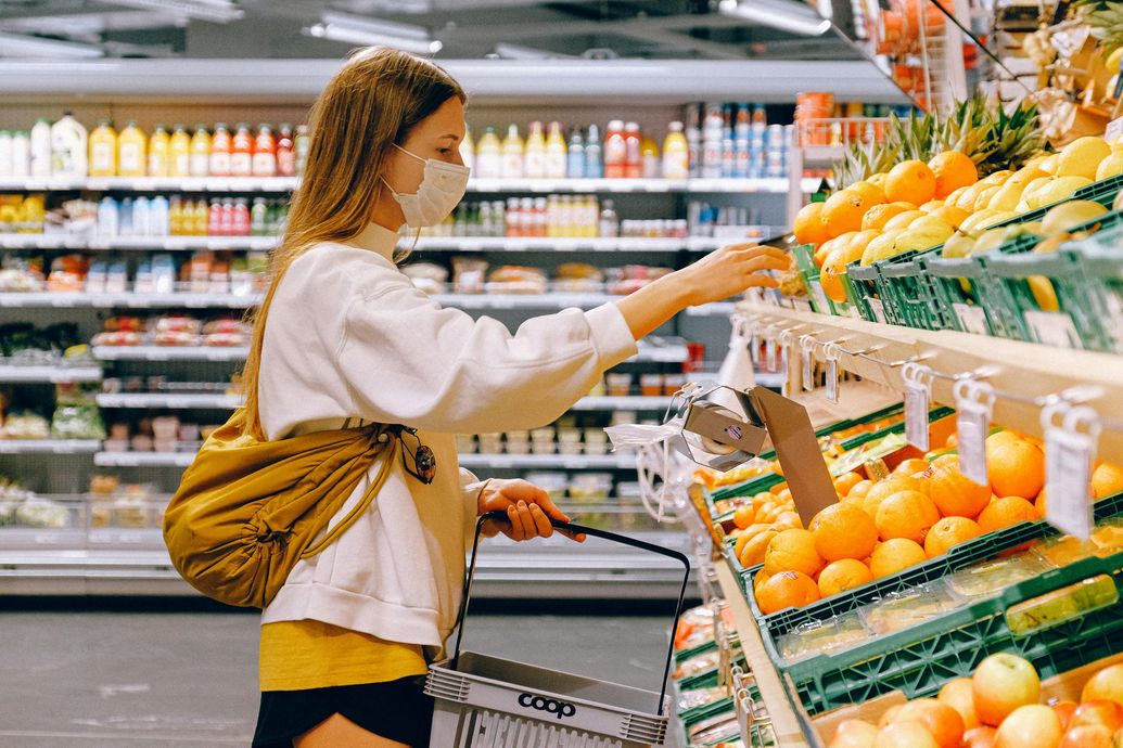A woman wearing a mask is shopping in a grocery store.