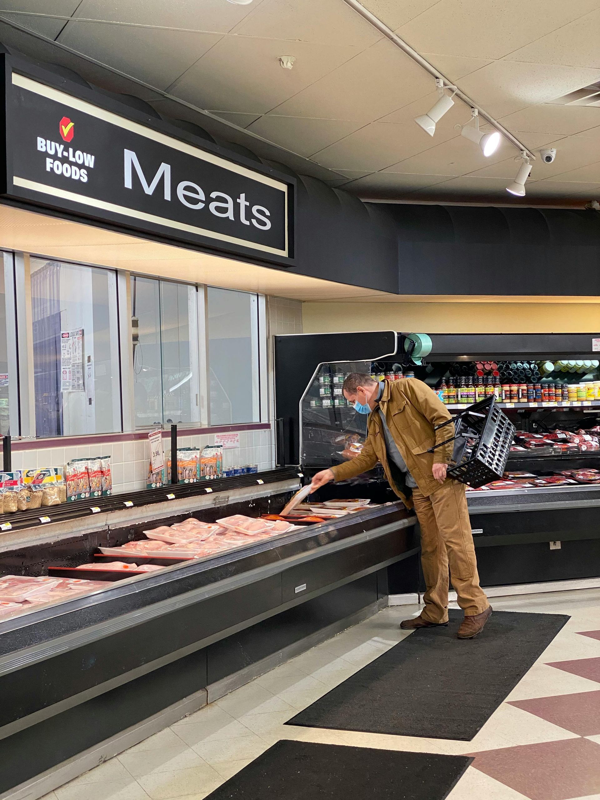 A man is standing in a meat section of a grocery store.