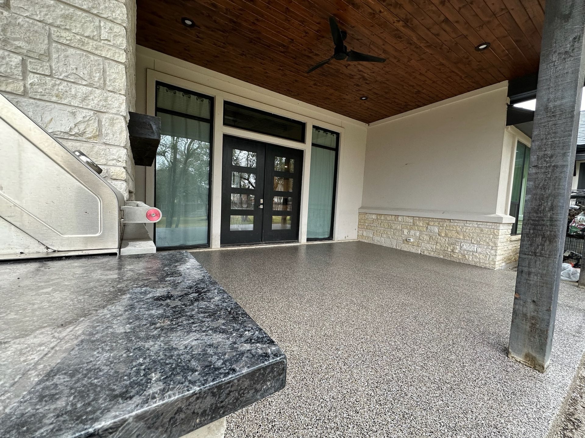 A patio with a ceiling fan and a stainless steel grill.