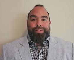 A man in a suit shakes hands with another man in a blue shirt