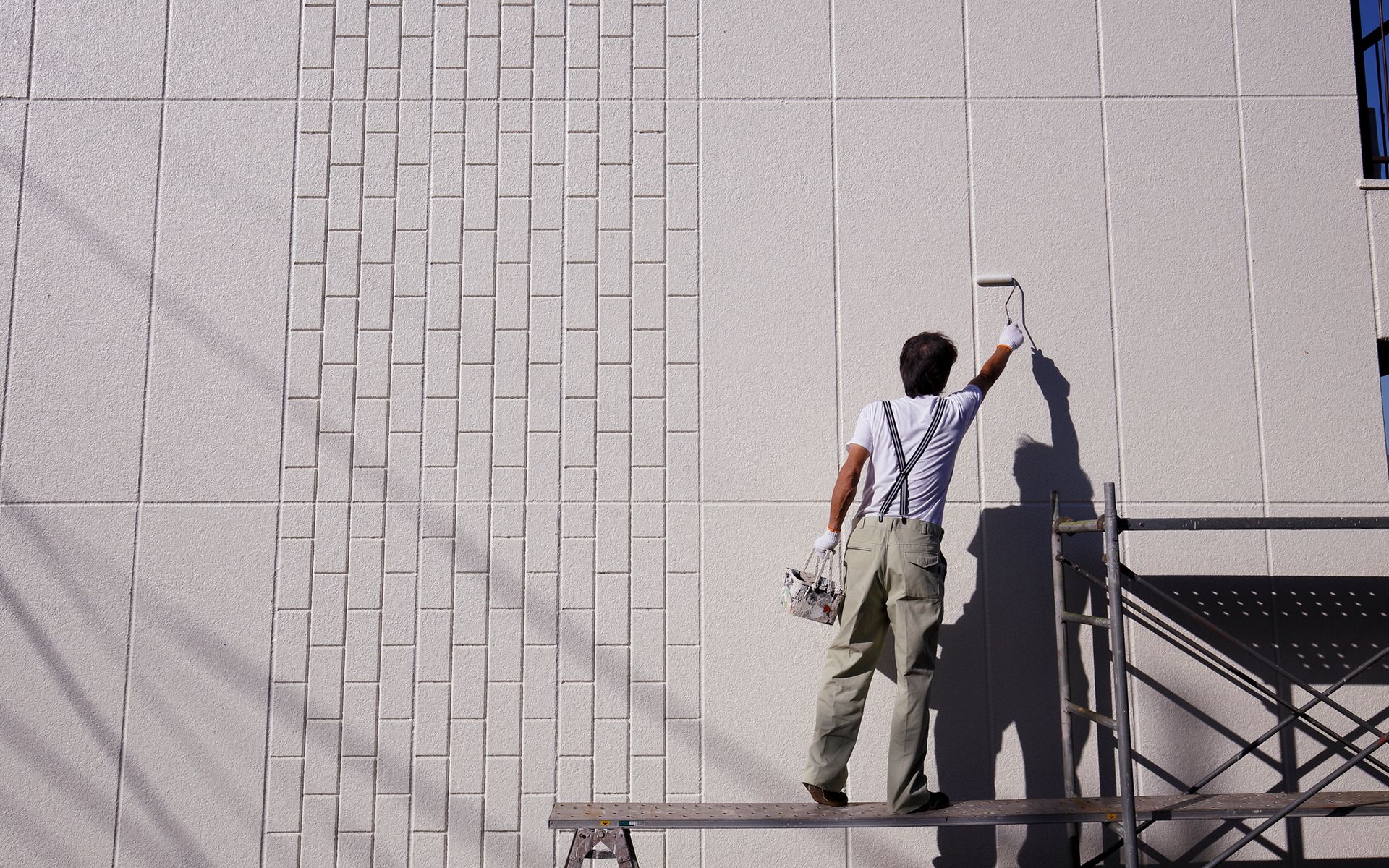 A man is standing on a scaffolding painting a wall.