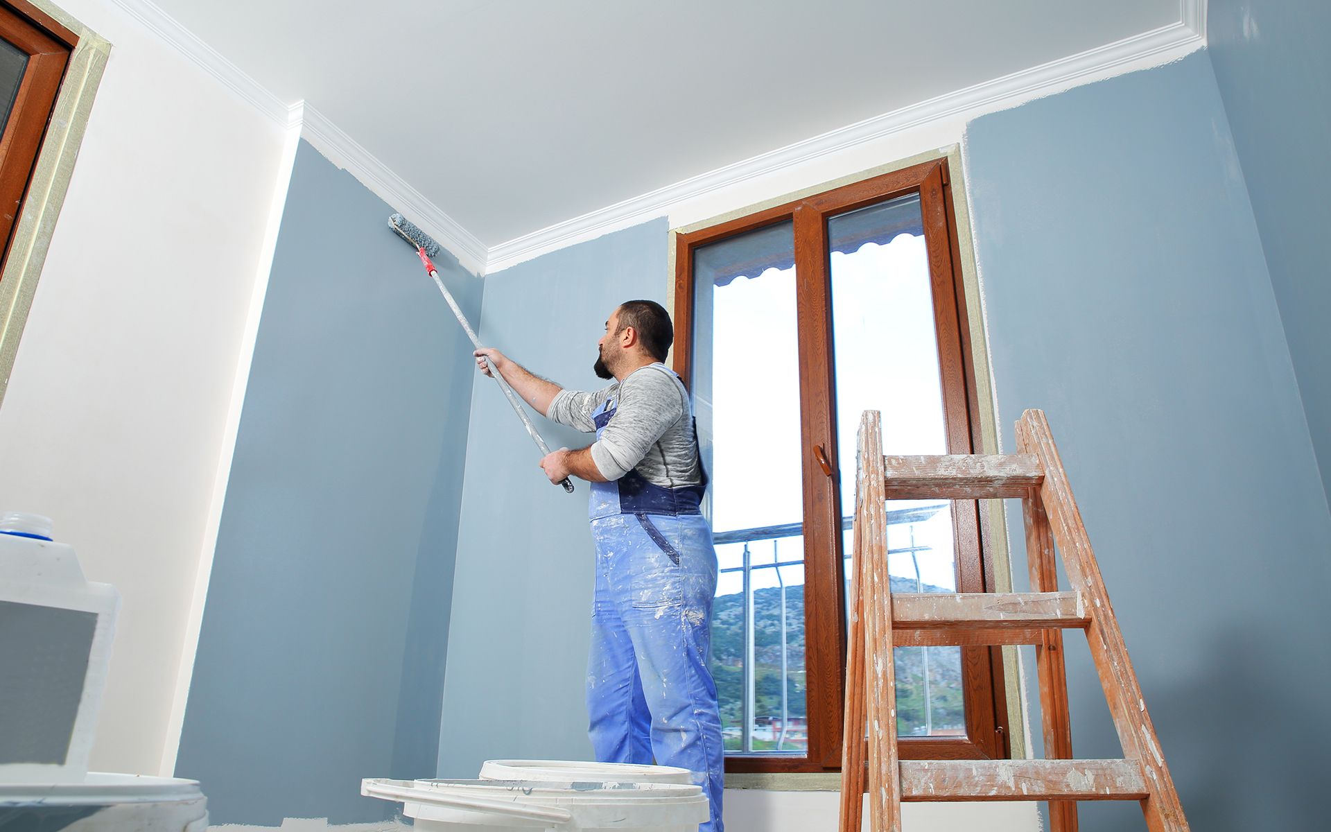 A man is painting a wall in a room with a roller.