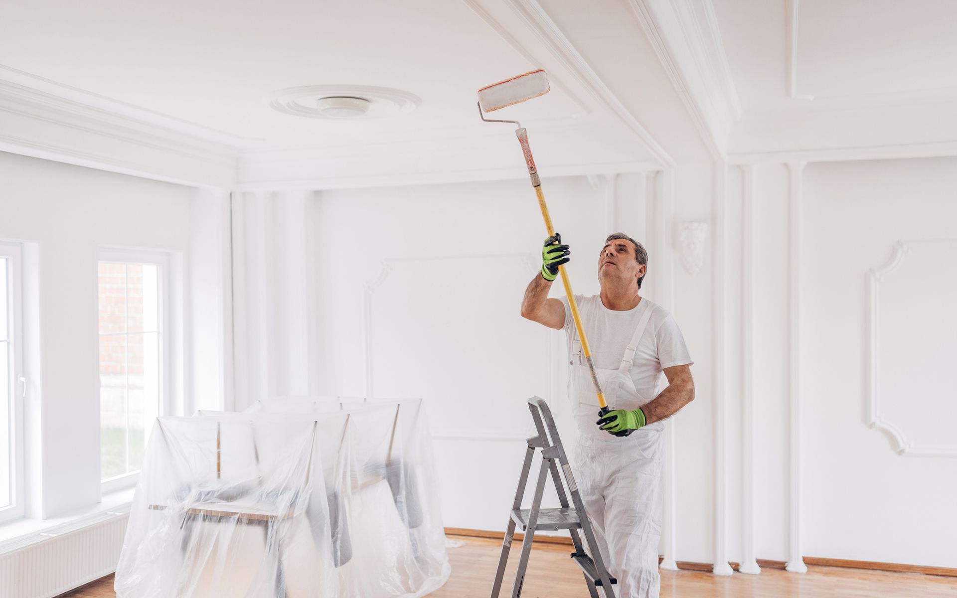 A man is painting the ceiling of a room with a paint roller.