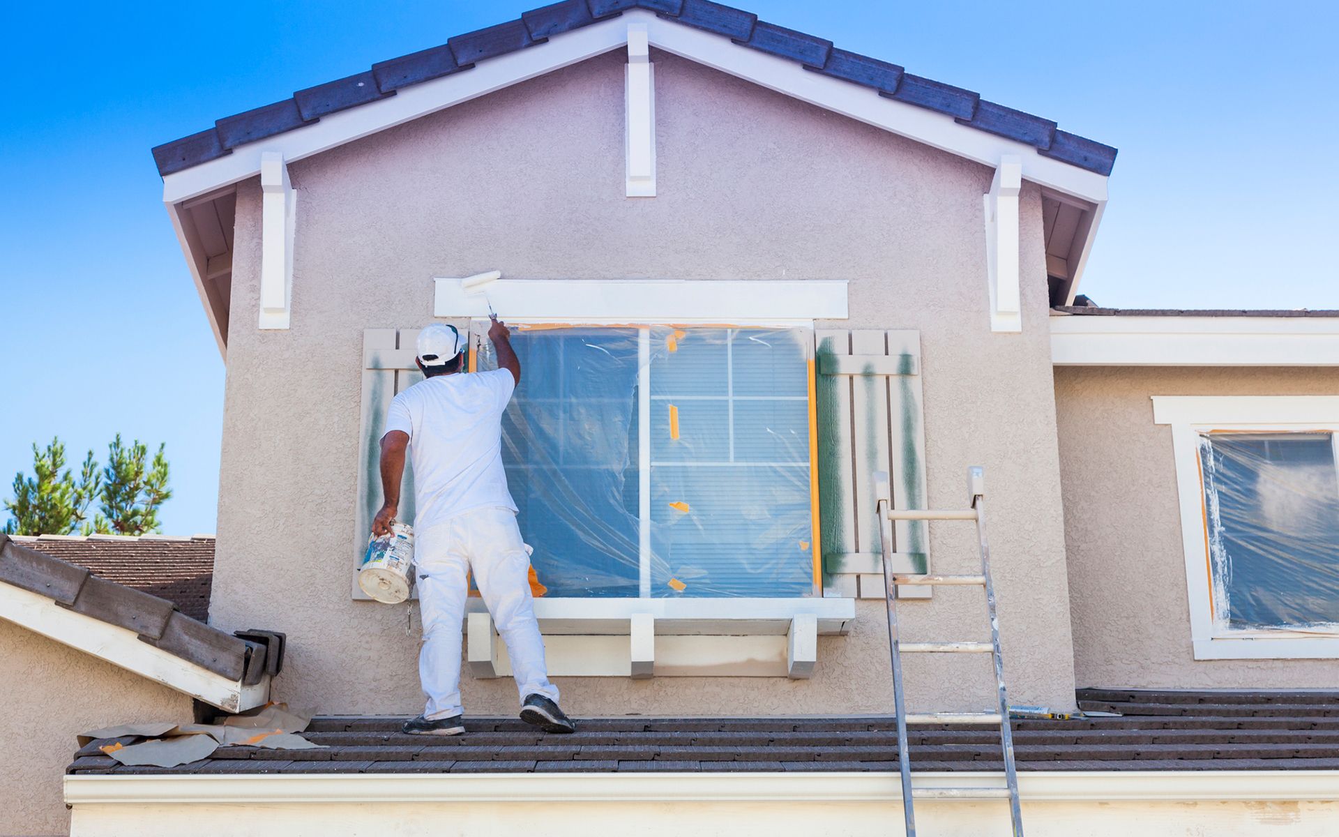 A man is painting a window on the side of a house.
