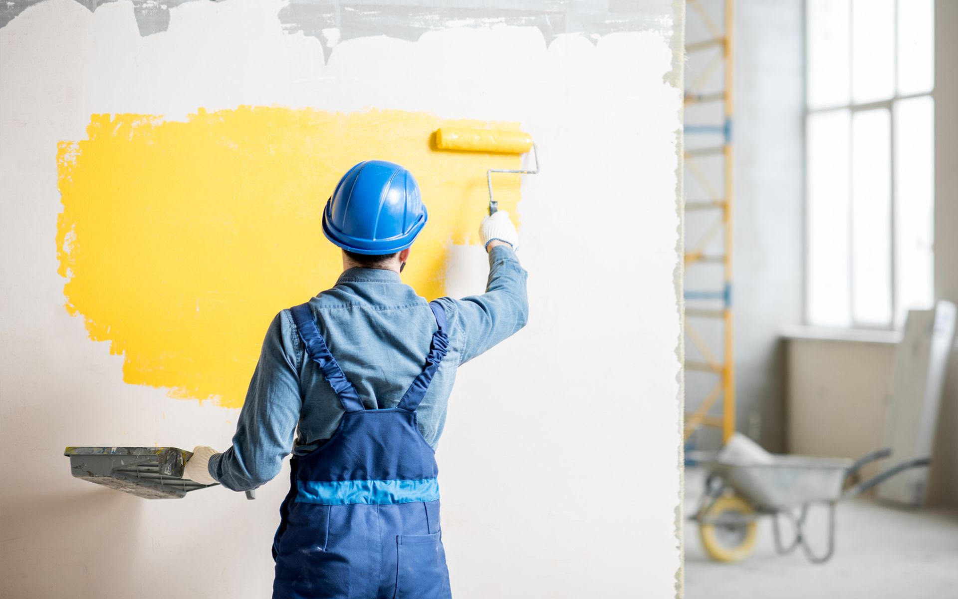A man is painting a wall yellow with a roller.
