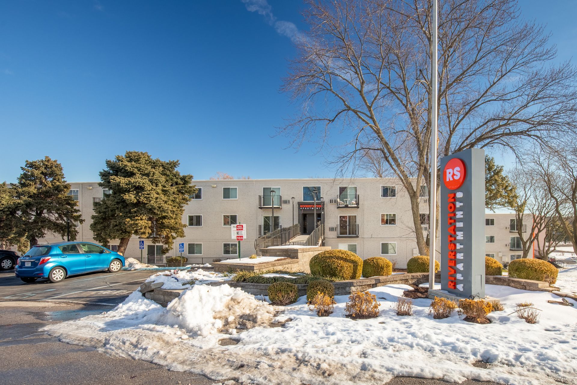 A blue car is parked in front of a building with snow on the ground.