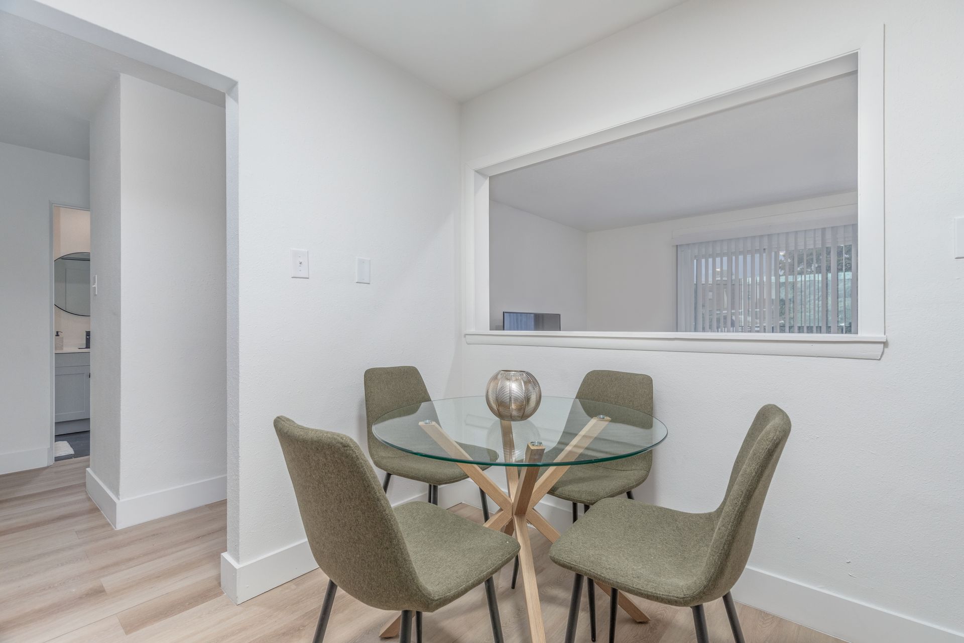 A dining room with a glass table and chairs and a window.