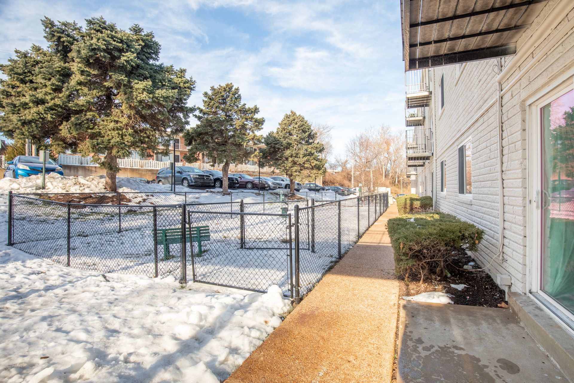A walkway leading to a snowy dog park in front of a building.