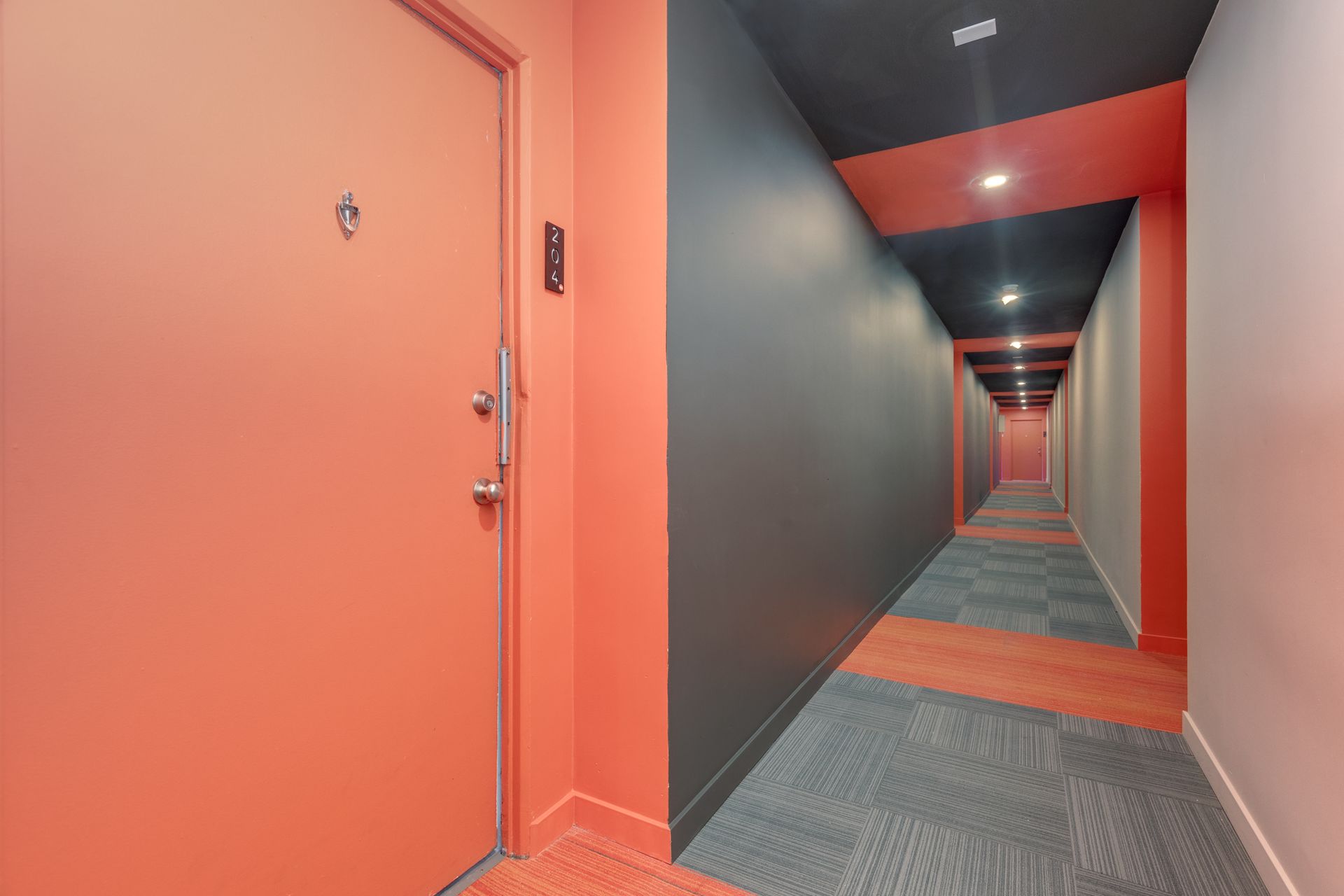 A long hallway with red and black walls and a door.