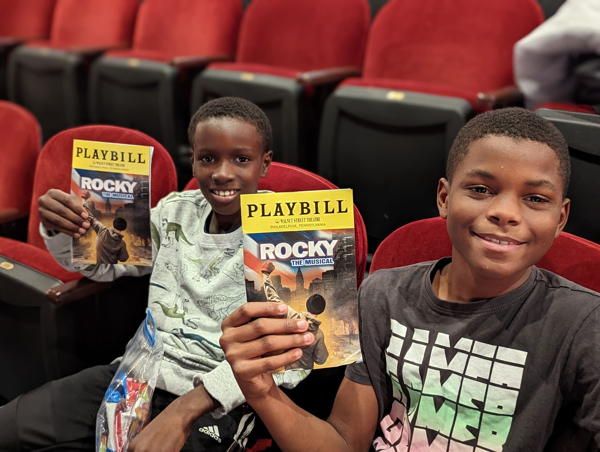 Two young boys are sitting in a theater holding rocky playbills.