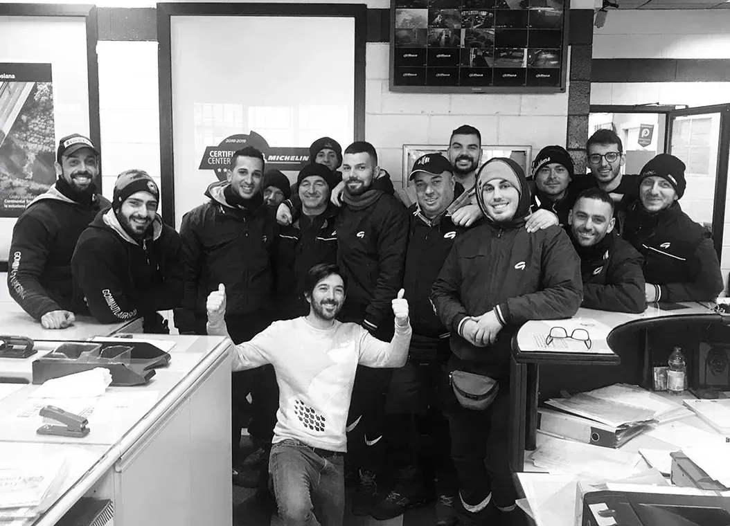 Un gruppo di uomini sorridenti in un laboratorio, alcuni con cappelli e giacche, abbracciati.
