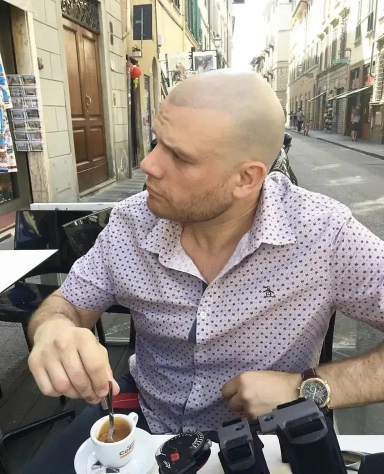 A man is sitting at a table with a cup of coffee in front of him.