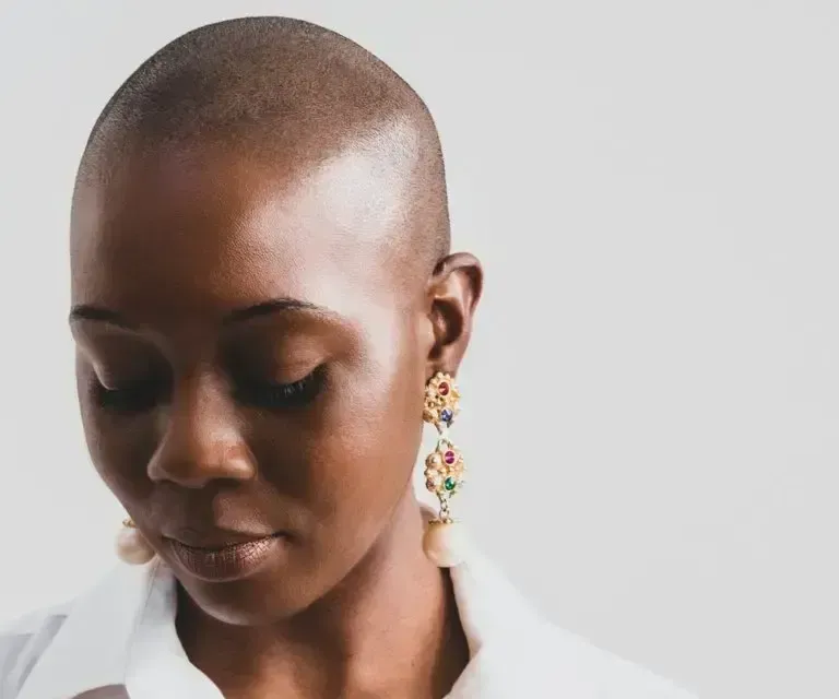 A woman with a shaved head is wearing earrings and a white shirt.