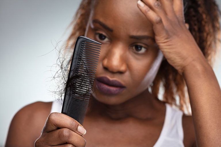 A woman is holding a comb and looking at her hair.