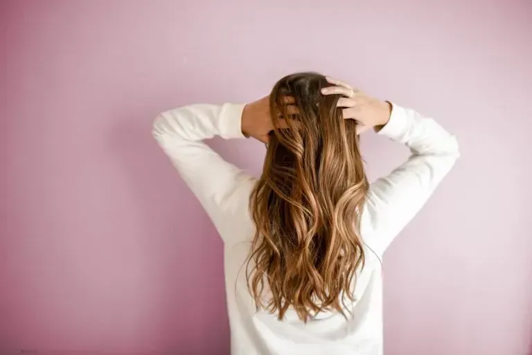 A woman with long hair is standing in front of a pink wall.