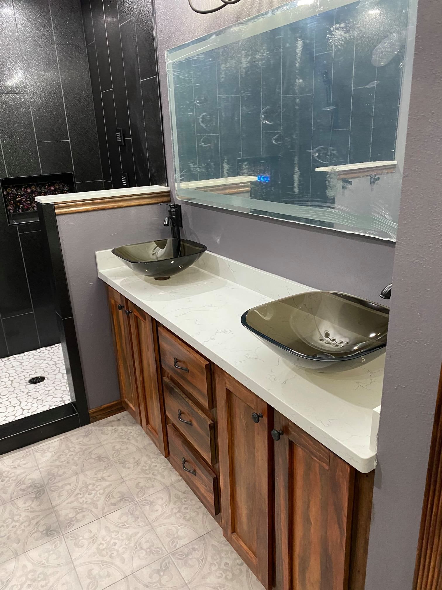 Bathroom vanity with double sinks, wooden cabinets, and a large mirror against black and white tiled walls