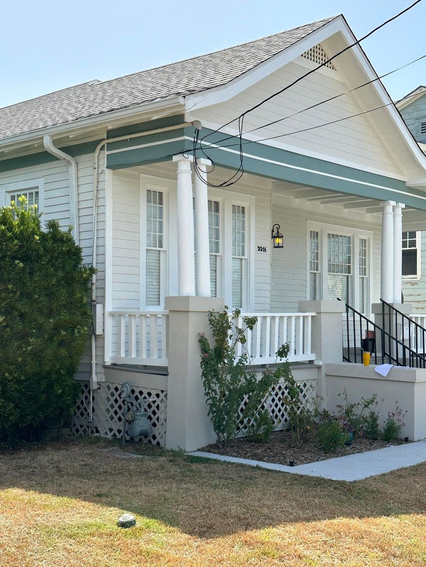 White house porch with a small front lawn, steps, and railing on a sunny day