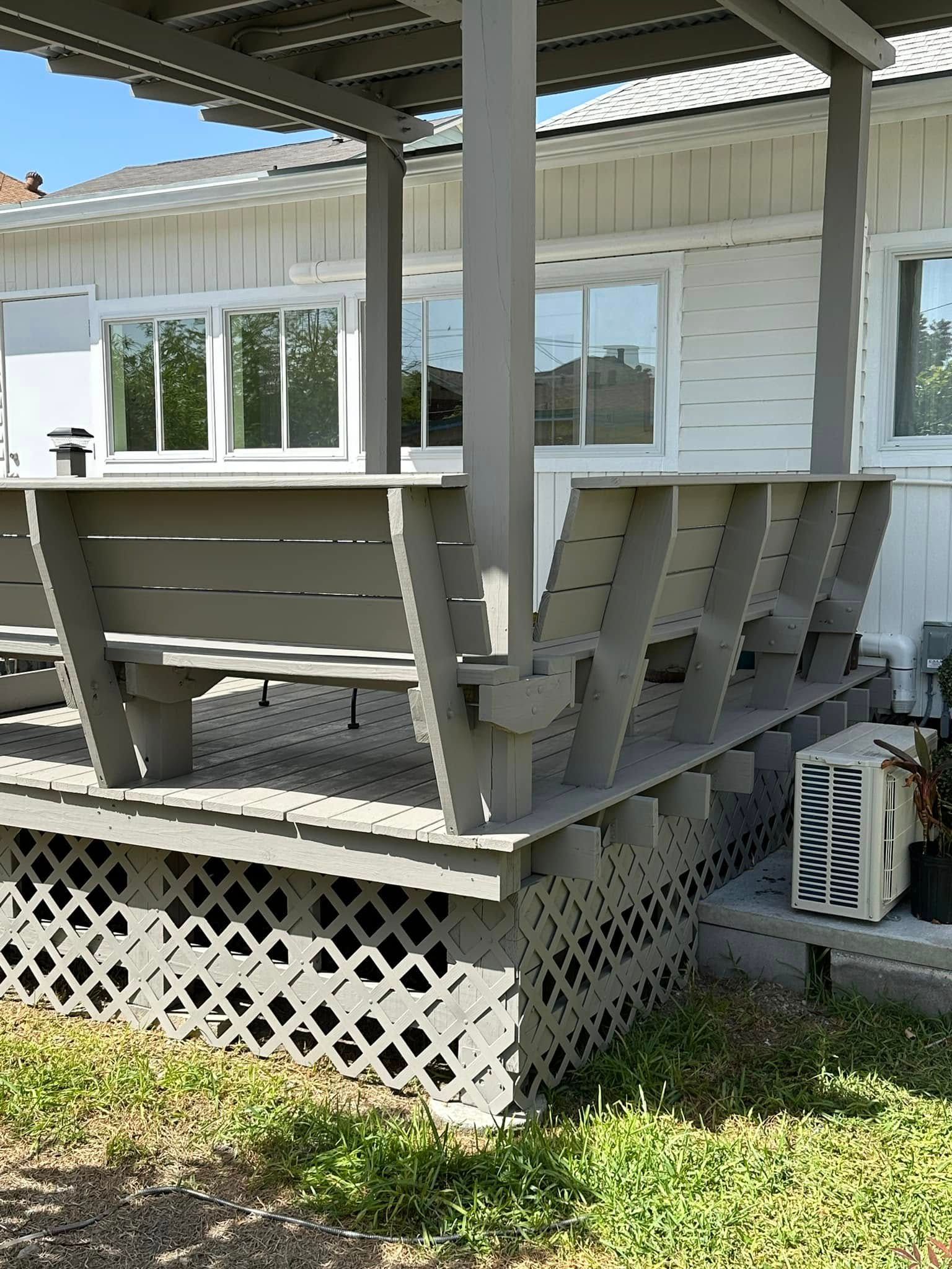Gray wooden porch with railing and lattice skirting beside a white house under a roofed canopy