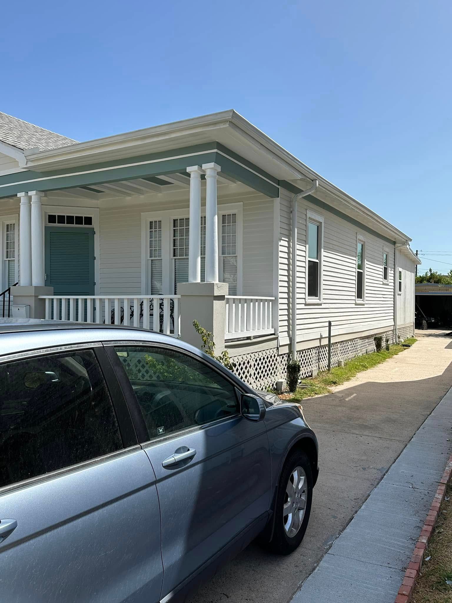 Silver car parked beside a white house with a porch on a sunny day