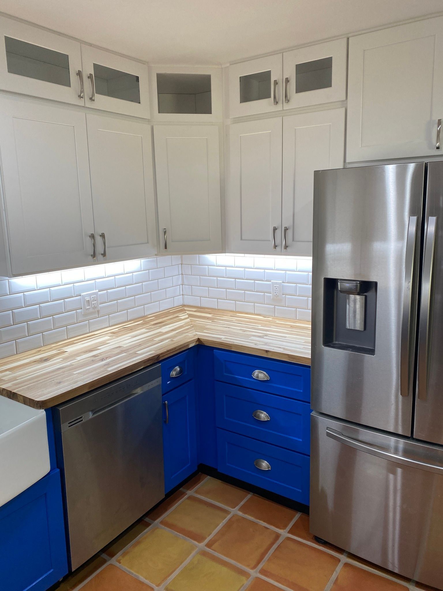 Small kitchen with white cabinets, blue lower drawers, stainless steel appliances, and tiled floor.