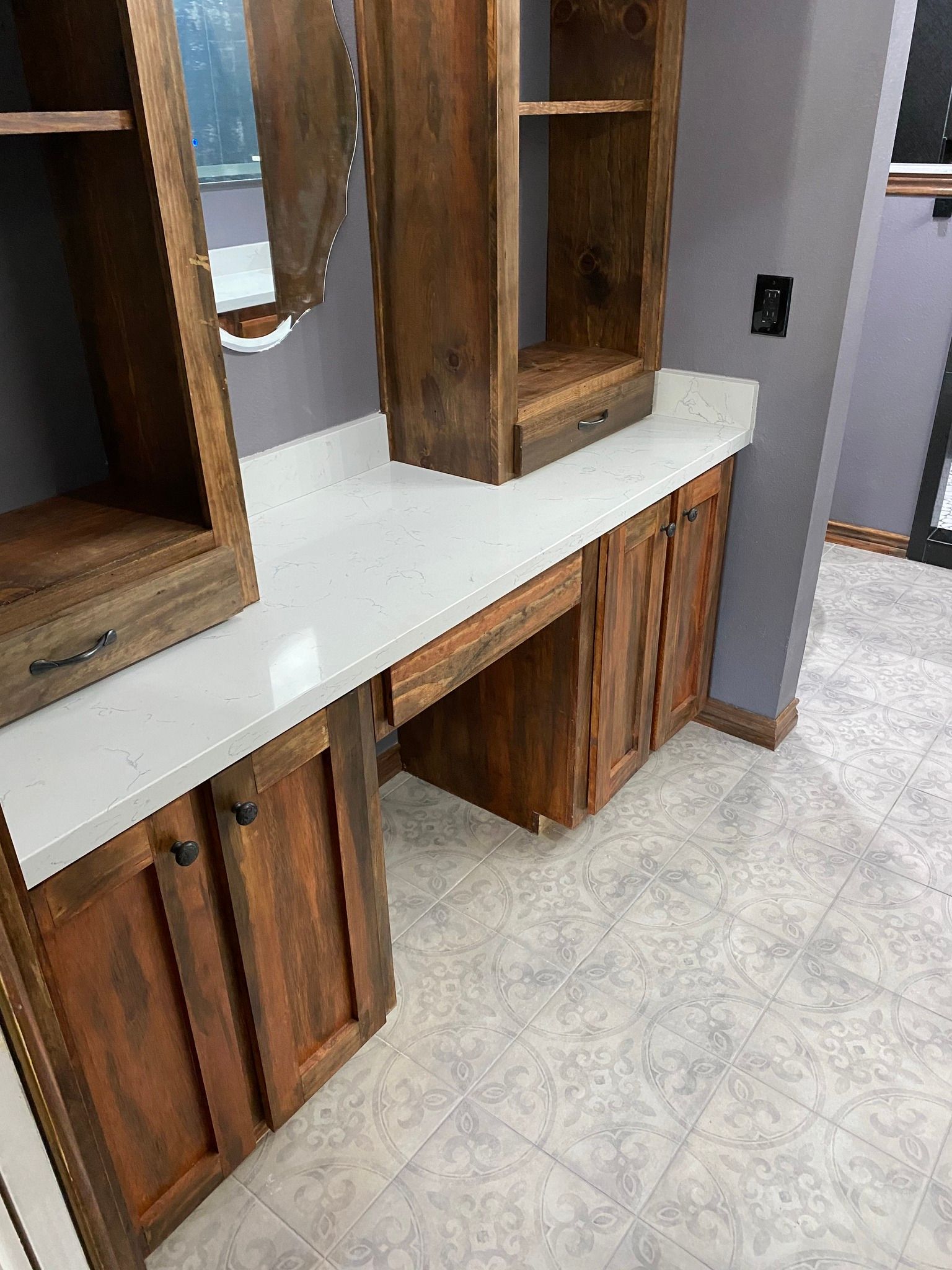 Wood vanity cabinet with mirrored shelves and a white countertop in a tiled room.