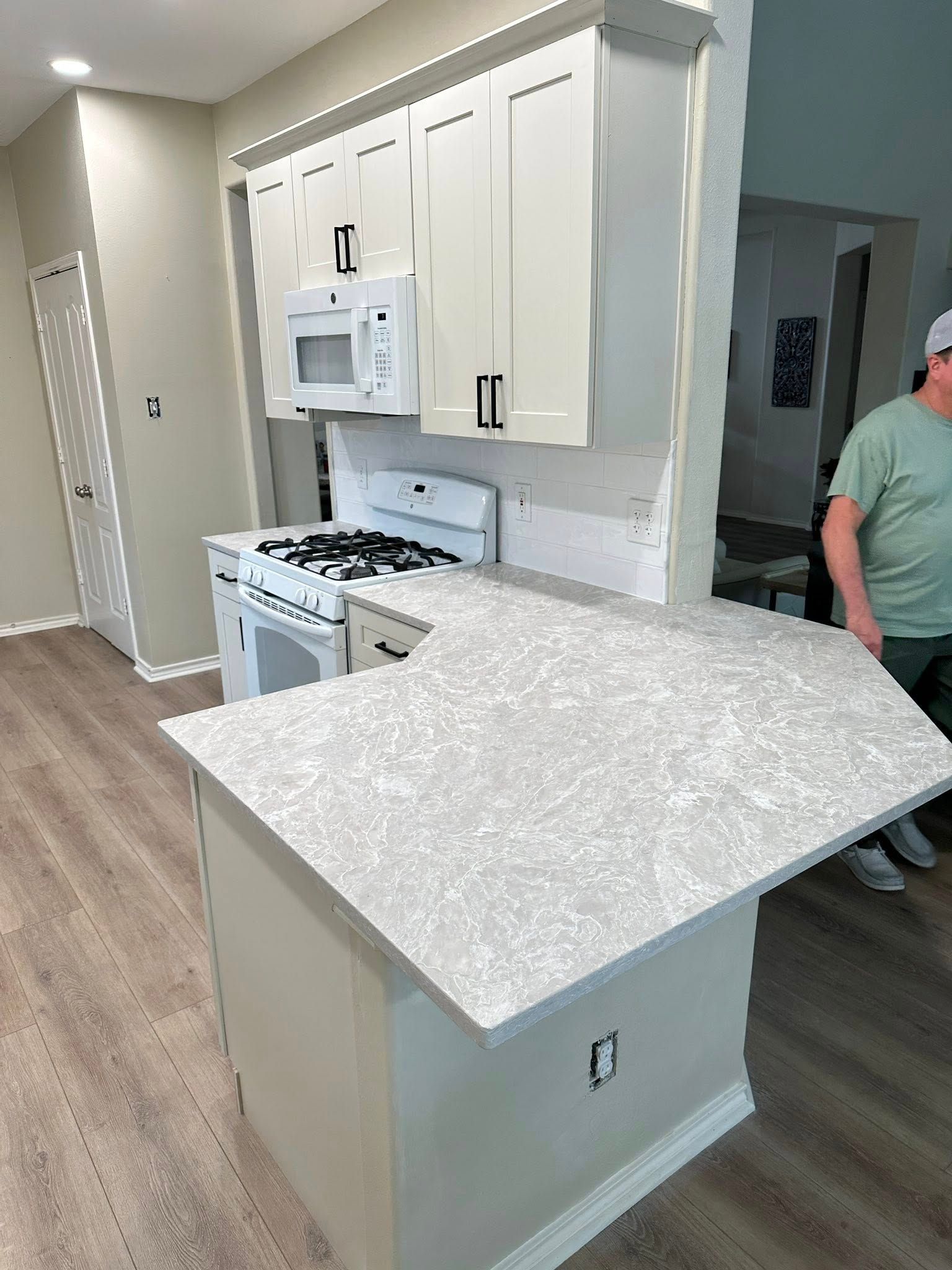 Bright kitchen with white cabinets, stove, island counter, and a man partially visible at right.
